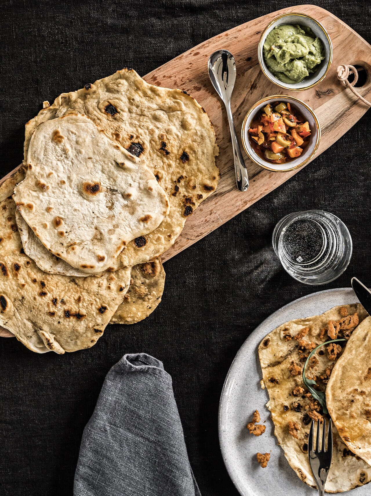 Tortillabröd på skärbräda med små skålar brevi